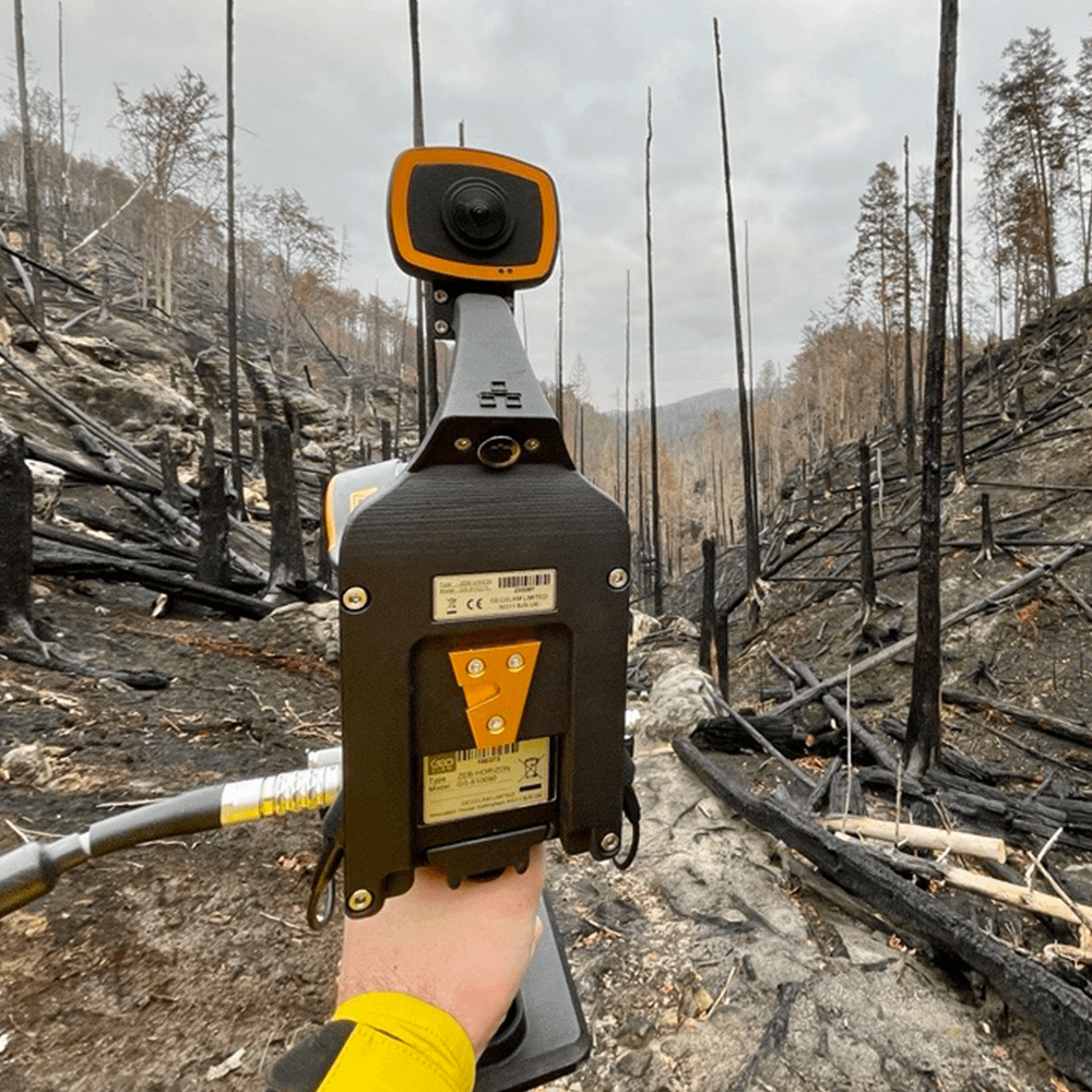 Mobile LiDAR scanner being held in front of burned trees