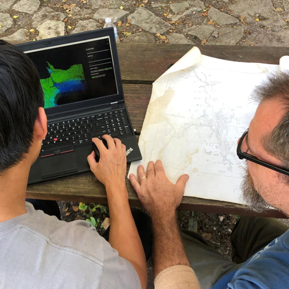 Two men looking at point cloud data on a laptop and blueprints